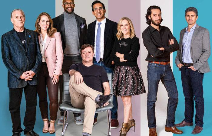 8 business people in business casual attire posing for a photon with a blue, pink and white striped background