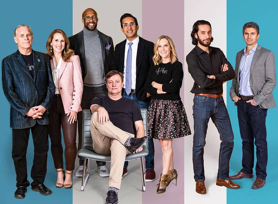 8 business people in business casual attire posing for a photon with a blue, pink and white striped background