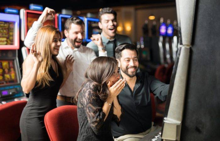 a group of five well dressed people are celebrating over a machine at a casino