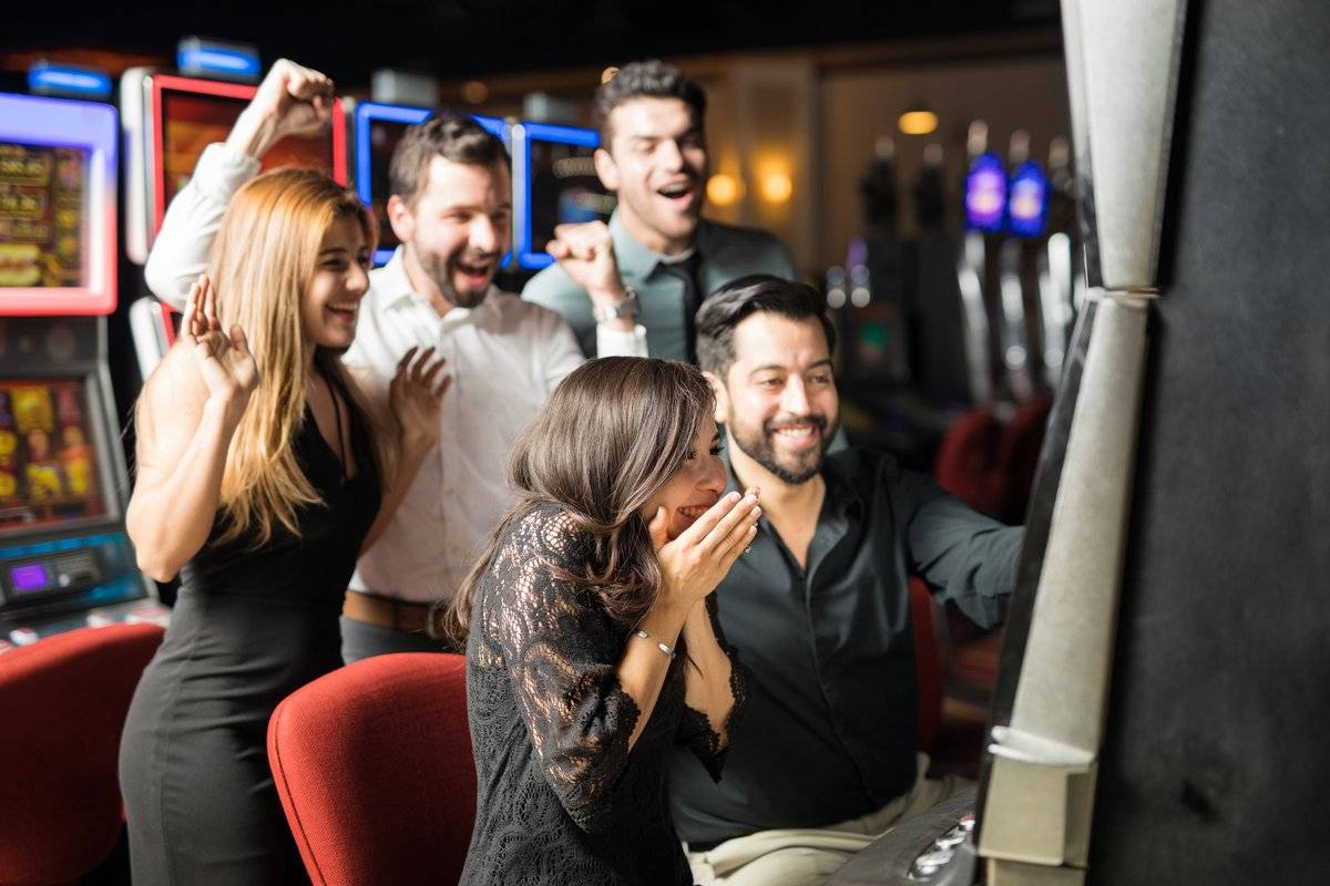 a group of five well dressed people are celebrating over a machine at a casino