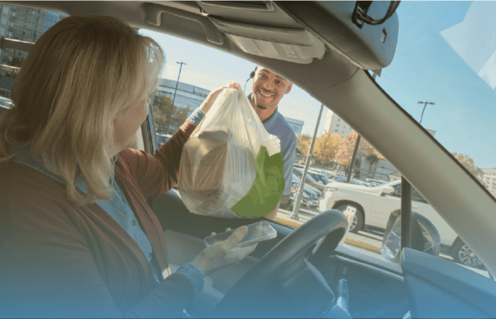 a retail employee hands groceries to a customer through her car window for curbside pickup