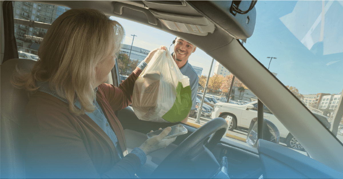 a retail employee hands groceries to a customer through her car window for curbside pickup
