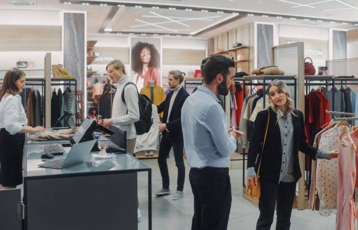 a retail boutique, with a line for the registers and an employee helping, and a woman getting help from an employee off to the side