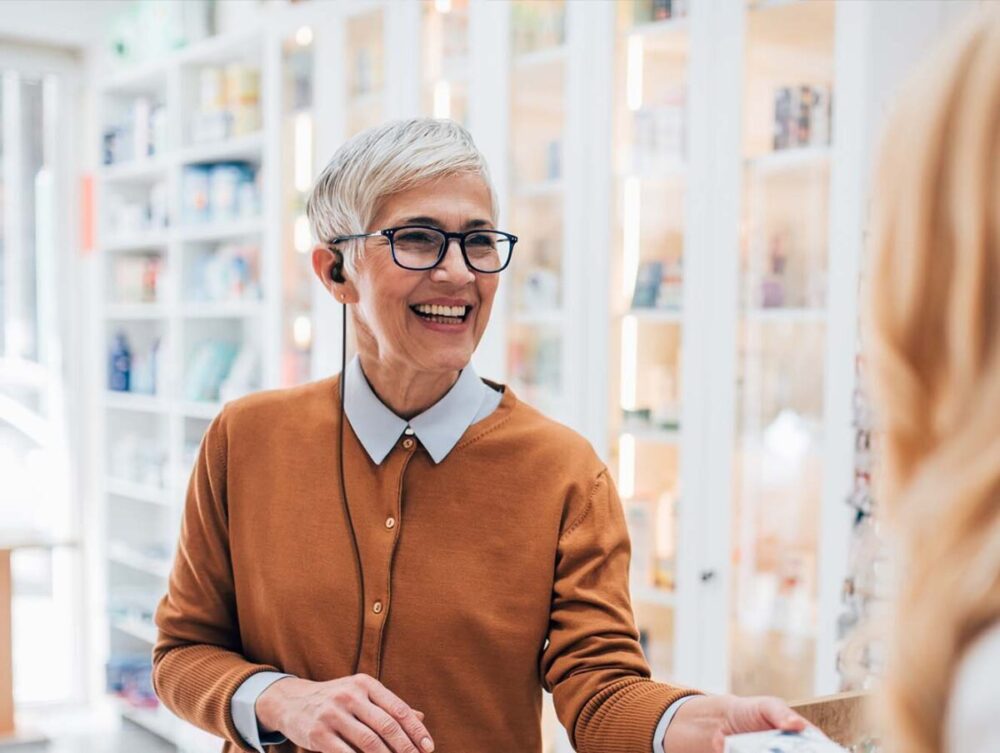A retail employee wearing an earpiece, is smiling while helping a customer