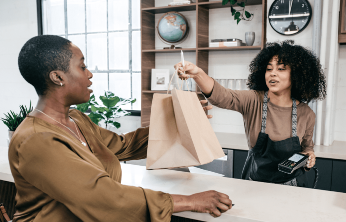 an african american employee smiling and handing a paper shopping bag over the counter to a customer