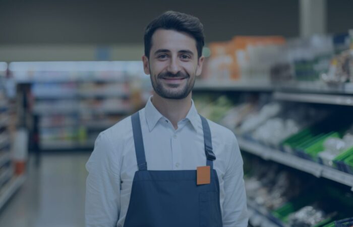 male retail worker wearing an apron and standing in a food aisle of a grocery store